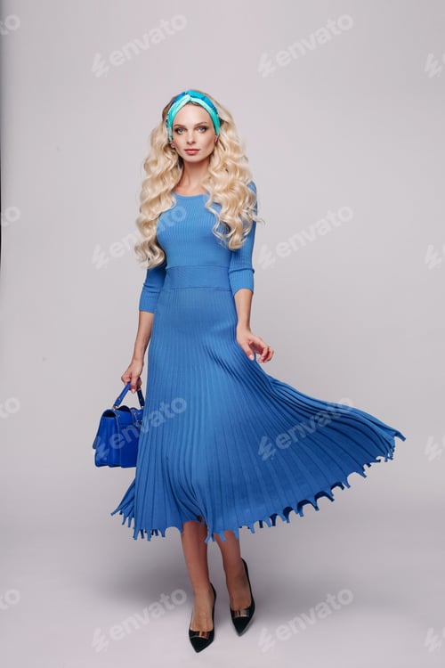 Preview: Glamour elegance young blonde woman in blue dress holding small bag at white studio background