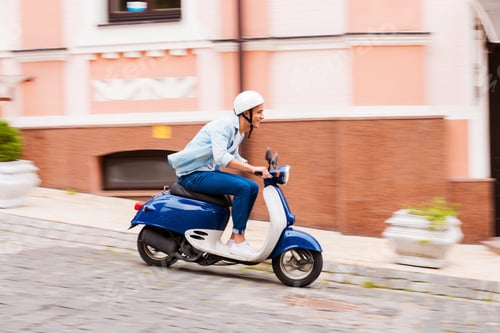 Preview: Scooter ride. Side view of young man in helmet riding scooter along the street and smiling