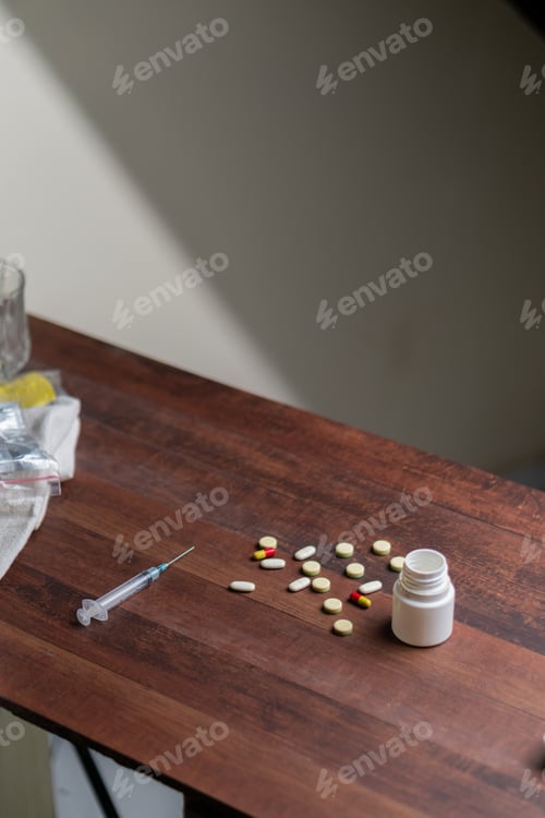 Preview: Scattered Pills and Syringe on Wooden Table