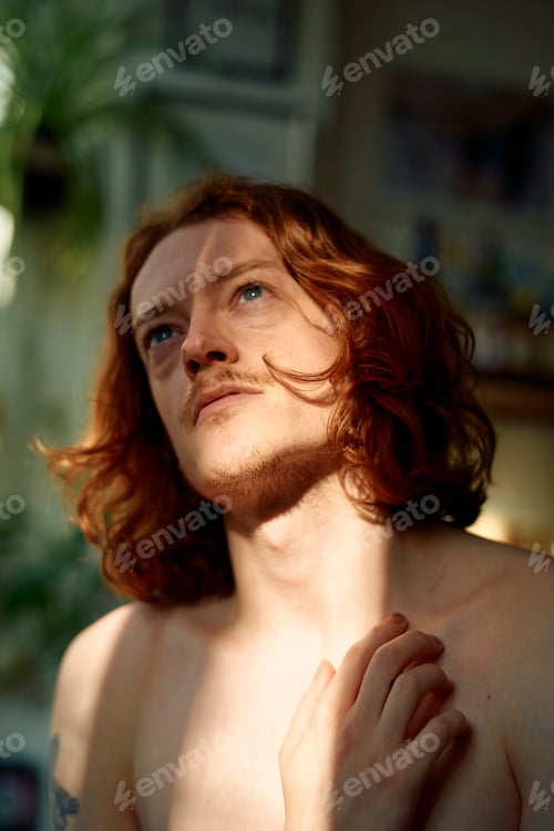 Preview: Shirtless young man with red hair gazing thoughtfully towards the light, caressing himself