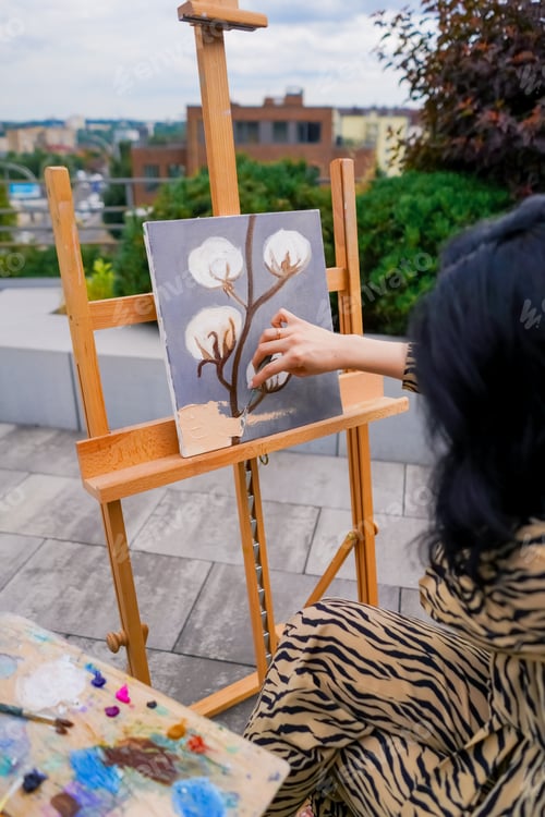 Preview: A young girl artist paints picture with a brush on a canvas that stands on an easel