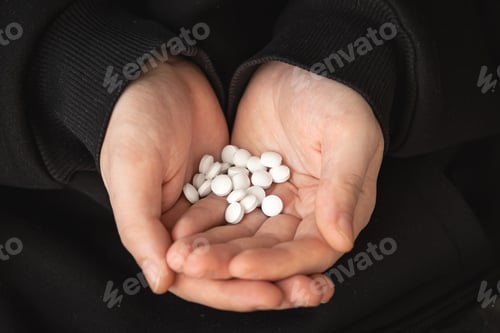 Preview: A lot of white pills in the hands of an adult man.