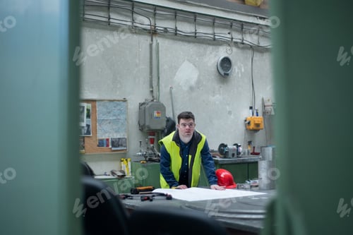 Preview: Young man with Down syndrome looking at blueprints when working in industrial factory, social