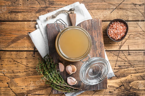 Preview: Bone broth for chicken soup in a glass jar. Wooden background. Top view