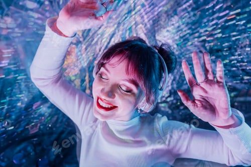 Preview: happy smiling woman with closed eyes and raised hands in white clothes and headphones dancing.