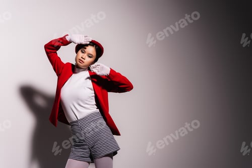 Preview: Trendy asian woman in gloves and beret looking at camera on grey background