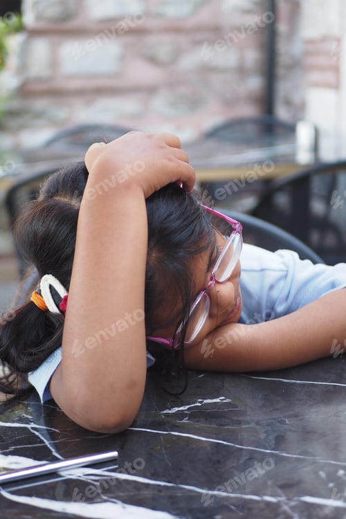 Preview: Child resting her head on a table at a casual outdoor setting