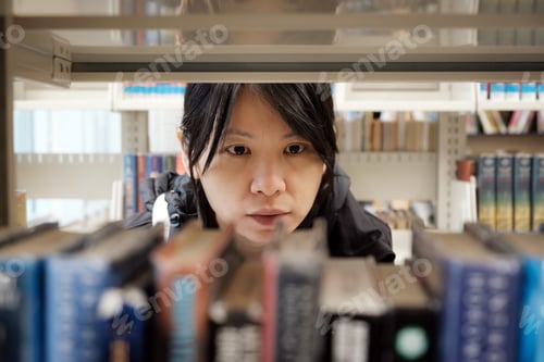 Preview: Portrait of serious Asian girl in library looking for a book