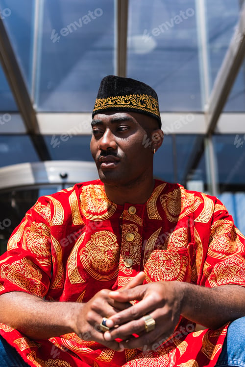 Preview: Thoughtful black man in traditional clothes and headdress near building