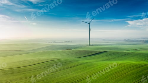 Preview: Foggy wind turbine on green field at sunrise