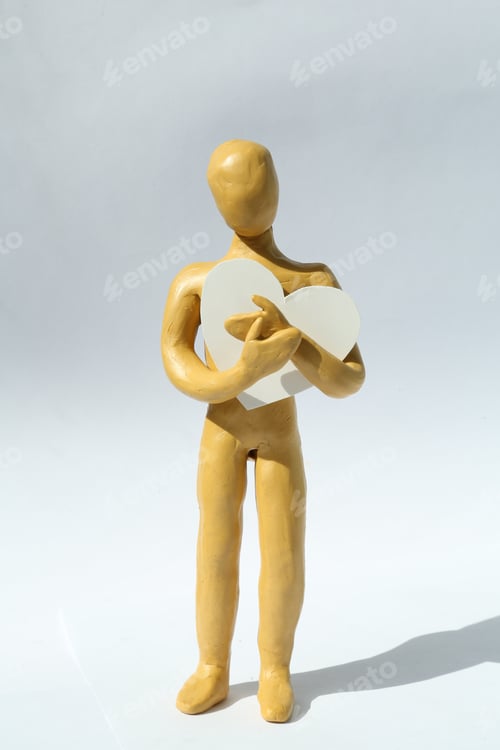 Preview: Yellow plasticine human figure with paper heart on white background