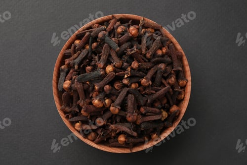 Preview: Aromatic dry cloves in wooden bowl on grey background, top view