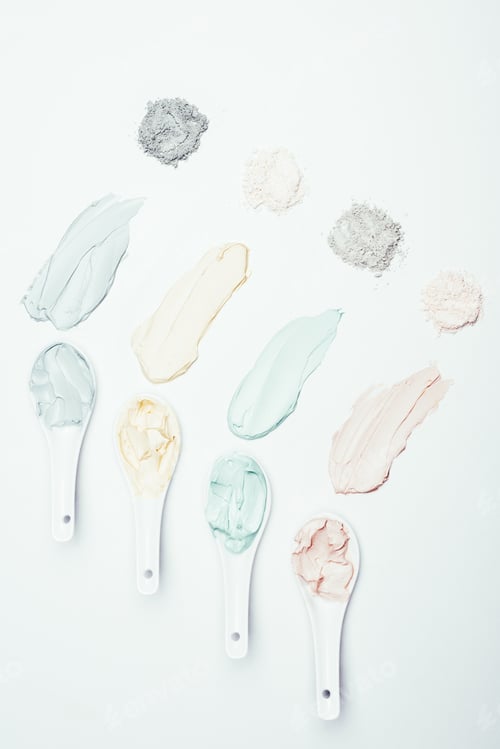 Preview: flat lay with spoons, different clay powder and colorful clay mask smudges placed in row on white