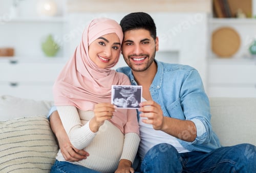 Preview: Happy pregnant muslim couple demonstrating baby sonography photo and smiling to camera