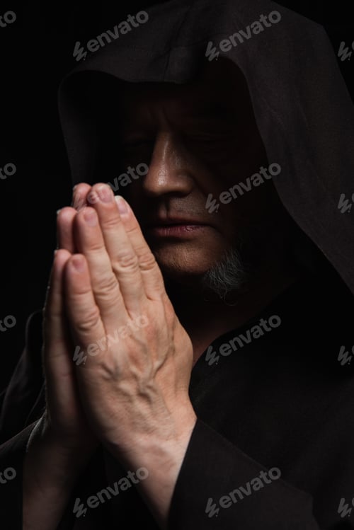 Preview: medieval monk with closed eyes and praying hands isolated on black