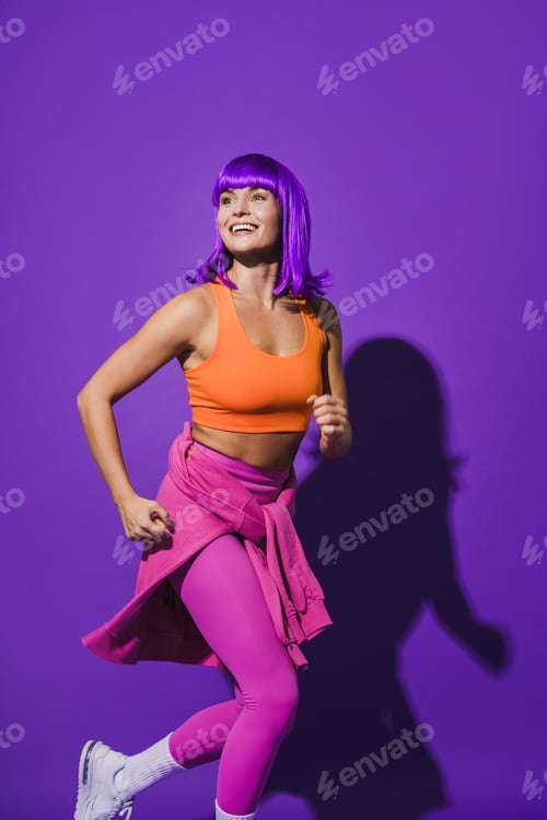 Preview: Cheerful woman wearing colorful sportswear running against purple background