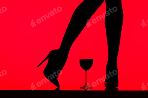 Preview: cropped view of black silhouette of girl in heels with glass of wine isolated on red