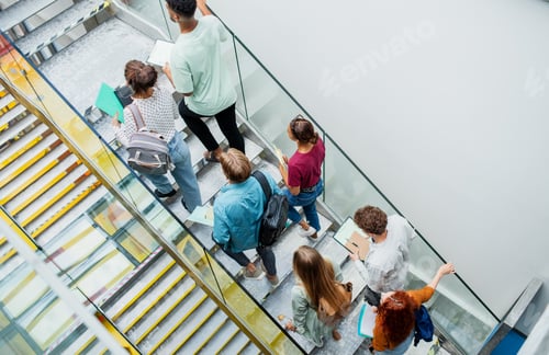Preview: Top view of university students walking up the stairs indoors, looking at camera and waving