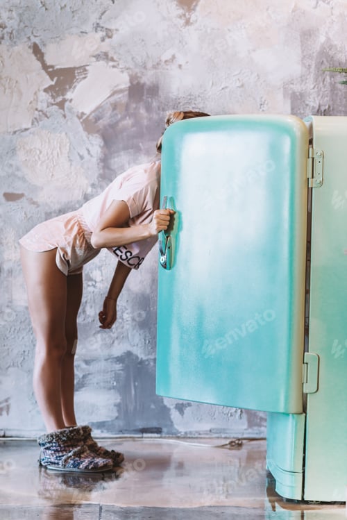Preview: Sexy woman in pink pajamas and slippers looks in the refrigerator and chooses products