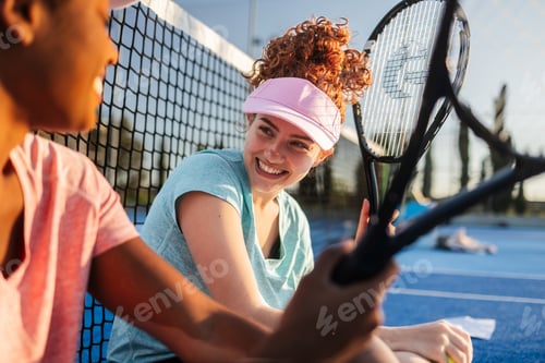 Preview: Two happy female tennis players chatting and smiling after match on a sunny day