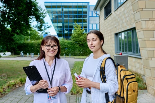 Preview: Teenage girl student talking to female teacher, outdoor, school building background
