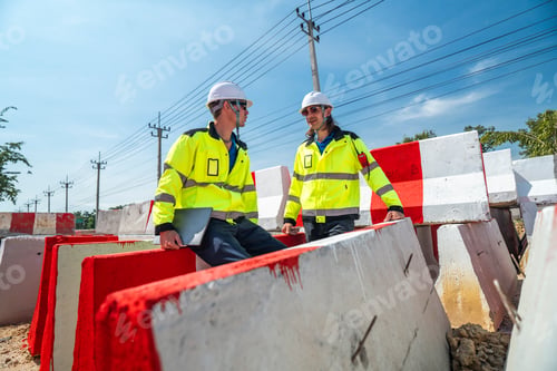 Preview: Two engineers sit amidst red-and white barricades at a construction site.