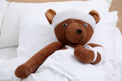 Preview: Toy bear with bandages lying in bed
