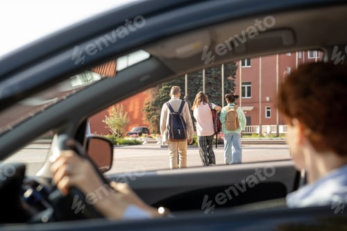 Preview: Young woman sititng in car and looking at group of schoolkids