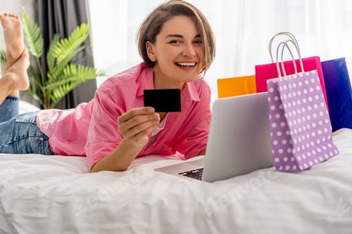 Preview: pretty happy woman lying on bed at home shopping online