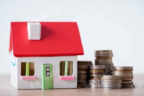 Preview: house model with red roof and white walls and stacks of metal coins isolated on grey