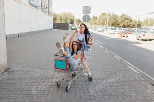 Preview: Two pretty slim dark-haired ladies,wearing casual outfit,have fun with a grocery cart near the
