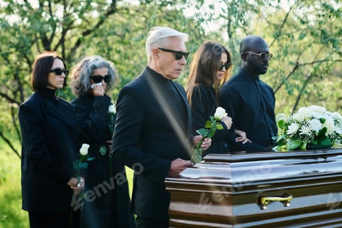 Preview: Friends and relatives of passed away person with white roses standing by coffin