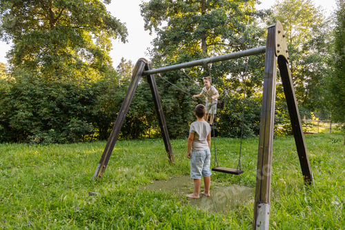 Preview: Two kids are having fun in a park on a swing set. One child swings happily