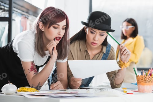 Preview: Multiethnic young fashion designers looking at sketch and discussing
