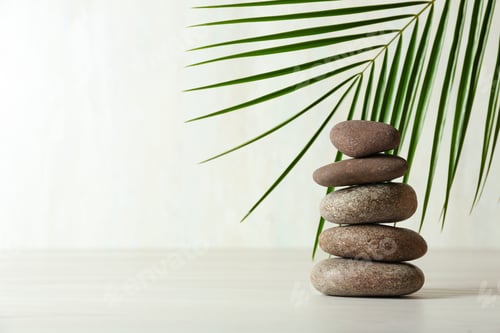 Preview: Stack of spa stones and palm leaf on table against white background, space for text