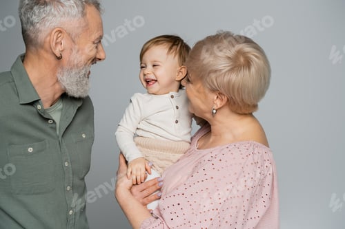 Preview: grandmother holding happy granddaughter near smiling bearded husband isolated on grey