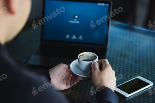 Preview: Fresh coffee for great ideas. Top view man working on laptop and holding cup of coffe while sitting