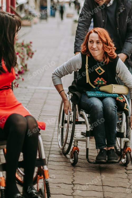 Preview: The girl is helped to ride in a wheelchair. Two girlfriends on wheelchairs in the city