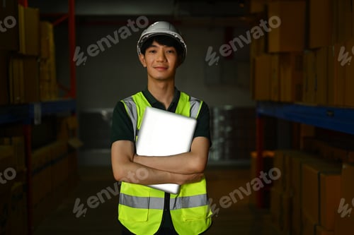 Preview: Confident male warehouse worker wearing safety vest holding laptop.