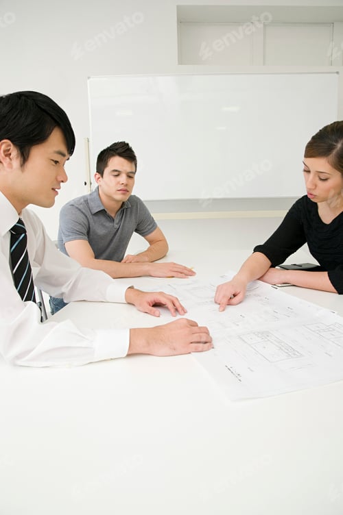 Preview: Three professionals engaged in a project discussion over blueprints.
