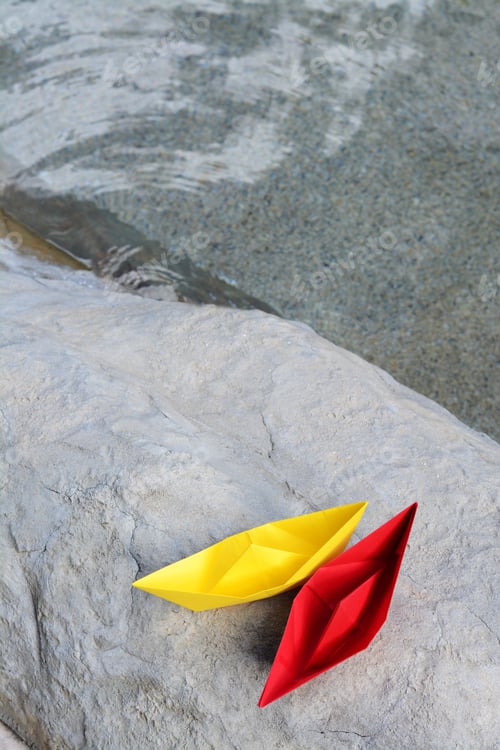 Preview: Beautiful yellow and red paper boats on stone near water outdoors, above view