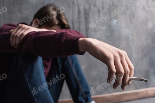 Preview: Close-up view of depressed teenage boy sitting with cigarette in hand