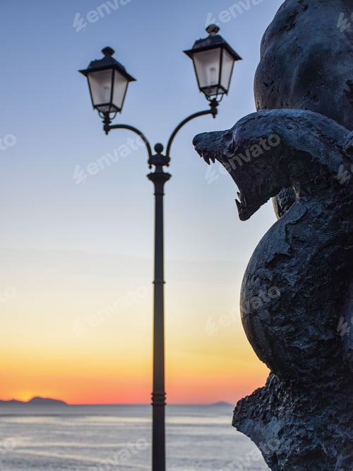 Preview: Closeup of a statue on a beach next to lamp posts at scenic sunset