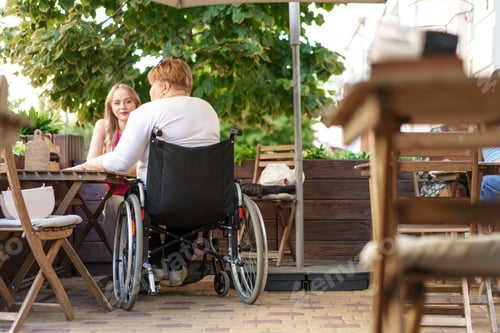 Preview: Mother with disability in wheelchair talking to her daughter while sitting at the table in cafe