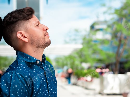 Preview: young Latino boy, with beard and short hair, is posing in profile leaning against a glass wall.