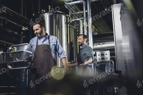 Preview: Male brewers in aprons working with industrial equipment at the brewery