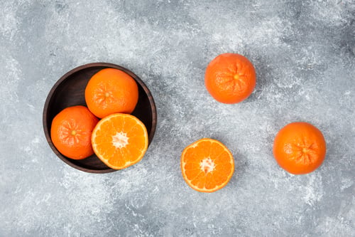 Preview: A wooden bowl full of juicy orange fruits on stone background