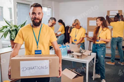 Preview: Portrait of a volunteer holding cardboard box with his colleagues in the background