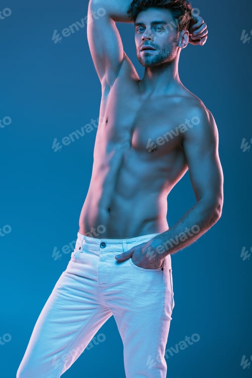 Preview: sexy, muscular man looking at camera while holding hand behind head isolated on blue
