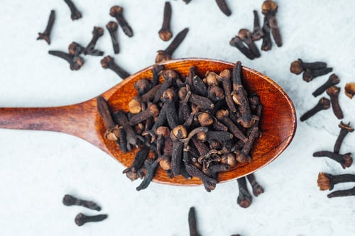 Preview: Cloves on a wooden spoon with scattered pieces on a light background